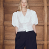 Woman wearing a white blouse and black shorts against a wooden paneled wall